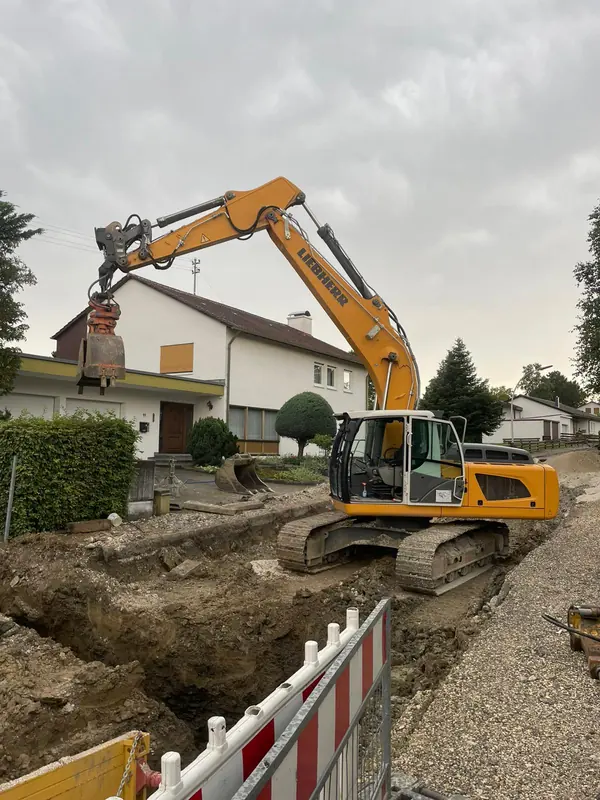 Liebherr Kettenbagger arbeitet an einem abgesperrten Leitungsgraben vor einem Wohnhaus
