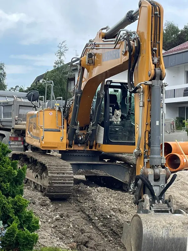 Kettenbagger neben bereitgelegten orangefarbenen Kanalrohren auf einer Wohnbaustelle