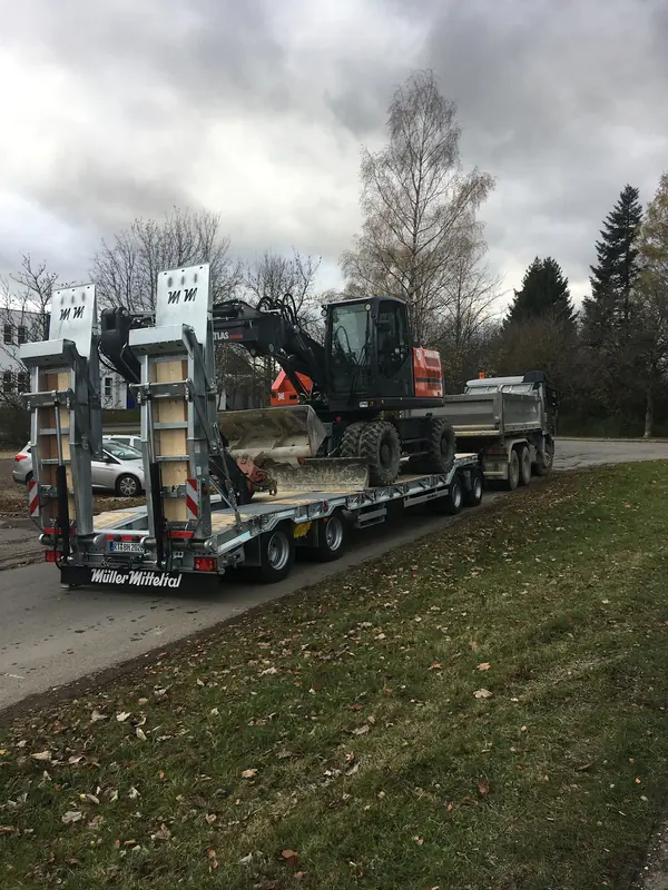 Tieflader mit Baumaschine und Kipperanhänger am Straßenrand