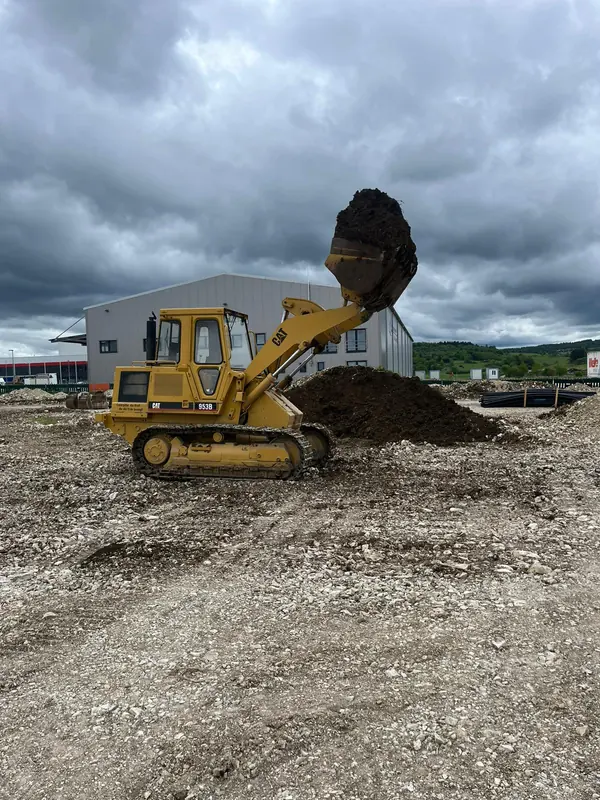 Laderaupe hebt mit gefüllter Schaufel Mutterboden auf einer Gewerbebaustelle an