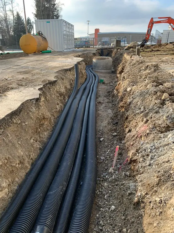 Mehrere gebündelte Leerrohre im offenen Leitungsgraben auf einer Gewerbebaustelle