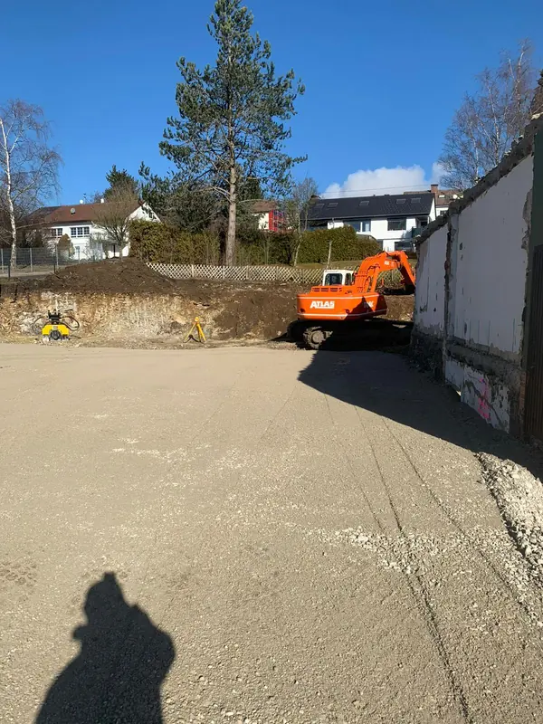 Fertig verdichtete Schotterfläche, am Rand ein Bagger beim Abschluss der Arbeiten