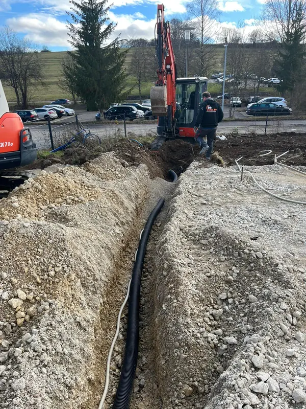 Schmaler Graben mit verlegtem Leerrohr entlang einer Parkplatzfläche