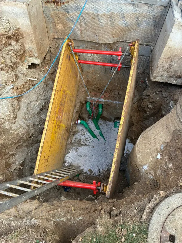 Tiefer, mit Verbau gesicherter Graben mit verlegten Wasserleitungen und Einstiegsleiter
