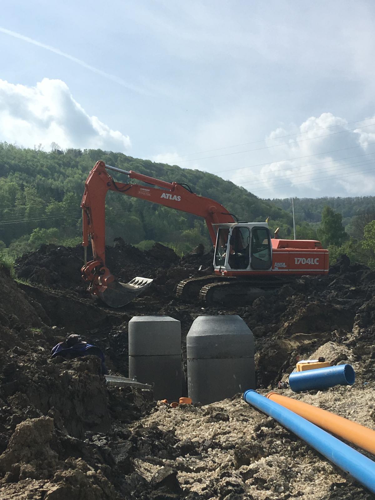 Kettenbagger im Erschließungsgebiet mit gesetzten Schächten sowie Wasser- und Kanalrohren